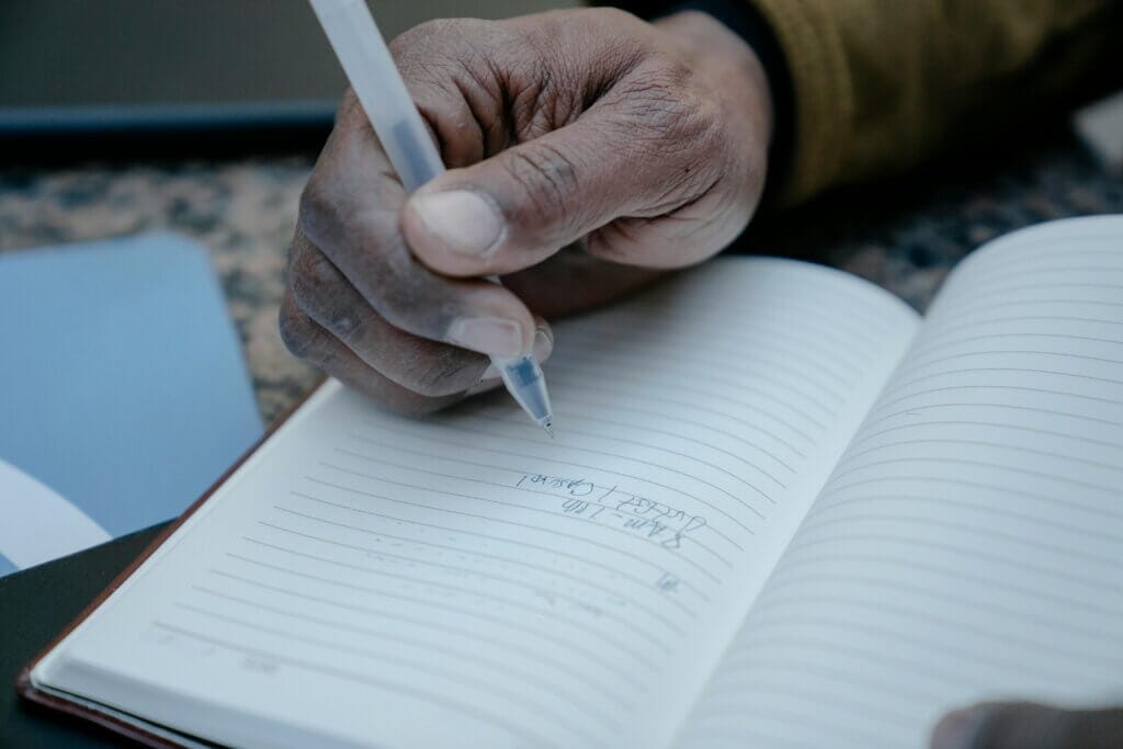 A close-up of a hand writing notes in a lined notebook with a pen.