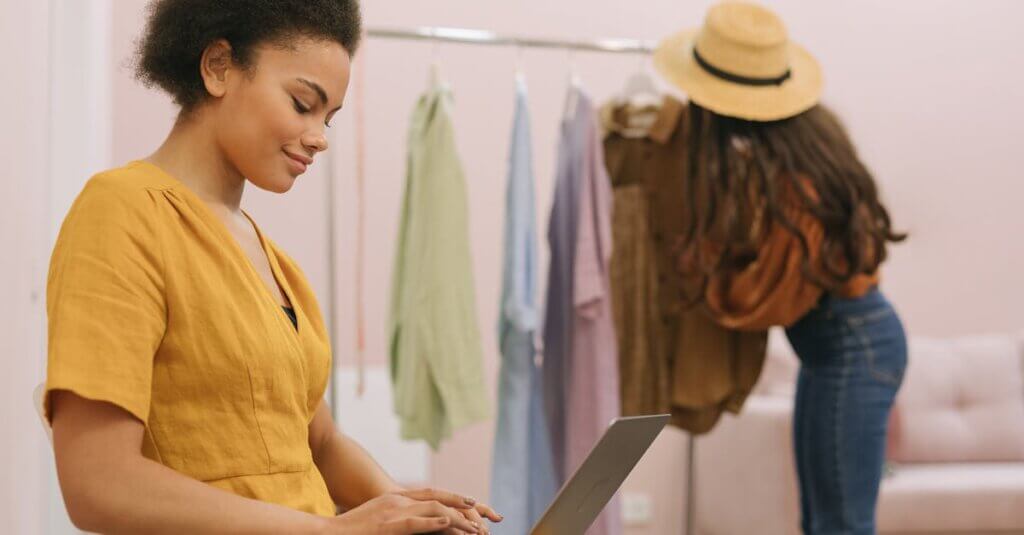 Woman in yellow dress working on laptop in small fashion boutique.